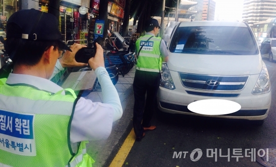 서울시 주차단속원들이 도로변에 불법주차 돼 있는 차량을 단속하기 위해 차량 사진을 찍고 있다. /사진=남형도 기자