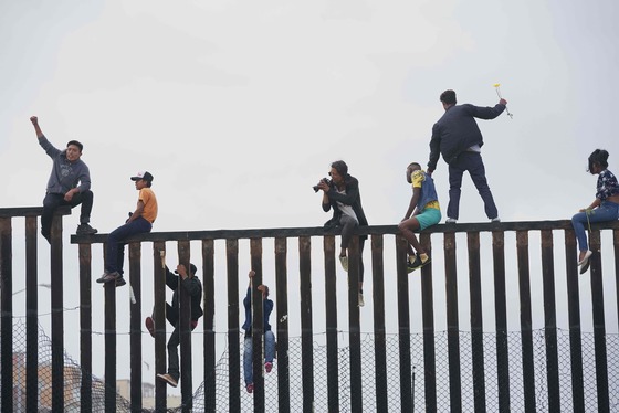  중미 캐러밴 난민들이 29일(현지시각) 美-멕시코 국경도시인 캘리포니아 주 산 이시드로의 장벽에 올라가 입국허용을 요구하는 시위를 하고 있다. 미국 정부는 국경지대의 이민자들에 대한 체포 가능성까지 거론하면서 불법 입국에 대해 강하게 경고하고 나섰다. /AFP=뉴스1
