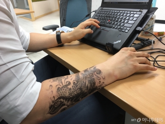 5일 오전 용무늬 타투 스티커로 타투를 한 뒤 출근한 기자가 책상에 앉아 일하고 있다./사진=남형도 기자
