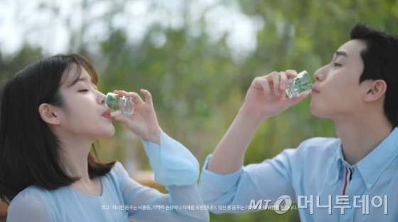 가수 아이유(왼쪽)과 연기자 박서준이 광고 속 소주를 마시는 장면. 술 광고에서 모델이 술을 마시는 행위 노출이 금지된다.