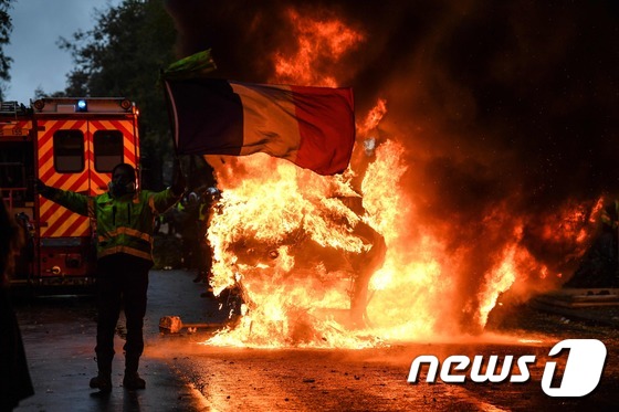 지난 1일(현지시간) 프랑스 파리에서 열린 '노란조끼' 시위에서 한 남성이 불타는 차량 앞에서 프랑스 국기를 든 채 에마뉘엘 마크롱 정부의 친기업 정책에 항의하고 있다.  © AFP=뉴스1