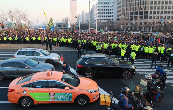주요 택시단체 조합원들이 지난달 20일 서울 여의도 국회의사당 앞에서 카풀 반대 집회를 개최한 뒤 마포대교 방향으로 행진하고 있다. 행렬 옆 도로로 한 택시가 지나치고 있다.<br>

