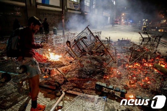 지난 19일(현지시간) 칠레 시위에 참가한 사람이 쇼핑카트 등에 불을 지르고 있다. @로이터=뉴스1