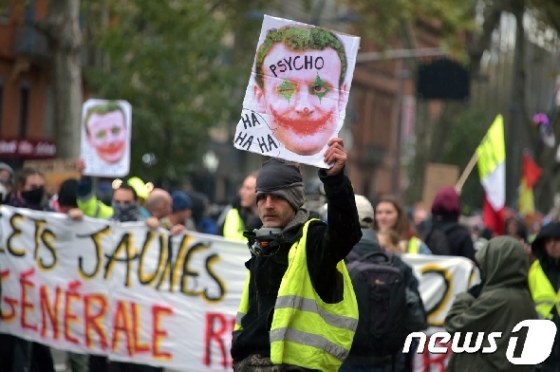 16일(현지시간) 프랑스에서 노란 조끼 1주년 시위가 열렸다. 한 시위 참가자가 에마뉘엘 마크롱 대통령 얼굴에 악당 캐릭터 '조커'를 합성한 그림을 치켜들고 있다. © AFP=뉴스1