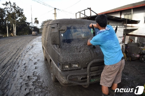 13일(현지시간) 필리핀 마닐라 남부 바탕가스주의 타나우안 타운에서 자동차 주인이 자동차에 쌓인 화산재를 닦고 있다. © AFP=뉴스1