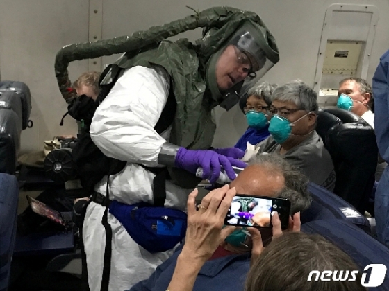 의료용 방호복과 산소 마스크를 착용한 미국 보건당국 관계자가 지난 17일 일본 하네다 국제공항에서 정부 전세기에 탑승한 국제 크루즈선 '다이아몬드 프린세스'의 미국인 승객들을 상대로 발열검사를 하고 있다. © 로이터=뉴스1