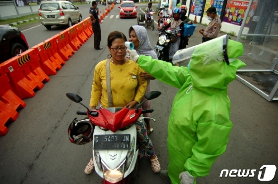 방역복을 입은 인도네시아 의료요원들이 태갈시내에서 통행인들이 열을 재고 있다. © 로이터=뉴스1