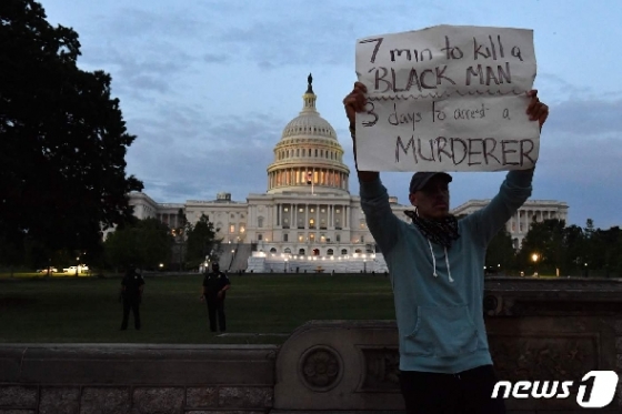 한 남성이 29일 미 국회의사당 앞에서 '한 흑인 남성을 살해하는 데는 7분, 살인자를 체포하는데는 3일이 걸렸다'고 쓴 미 정부를 비판하는 손팻말을 들고 있다. © AFP=뉴스1