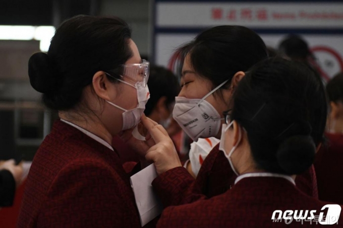 (베이징 AFP=뉴스1) 우동명 기자 = 24일 (현지시간) 베이징 공항 체크인 구역에서 코로나 19의 감염을 예방하기 위해 에어 차이나 승무원들이 마스크에 스마일 스티커를 붙여 주고 있다.   ⓒ AFP=뉴스1