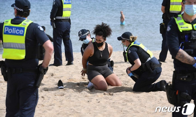 호주 멜버른의 한 해변에서 경찰에 코로나19 관련 봉쇄조치 반대 시위자를 에워싸고 있는 모습. © AFP=뉴스1