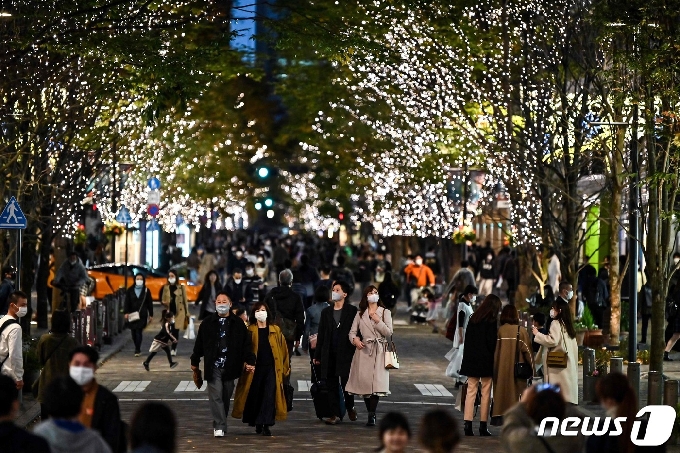 22일 도쿄의 한 거리에서 행인들이 전구로 장식된 가로수 아래를 지나가고 있다. © AFP=뉴스1