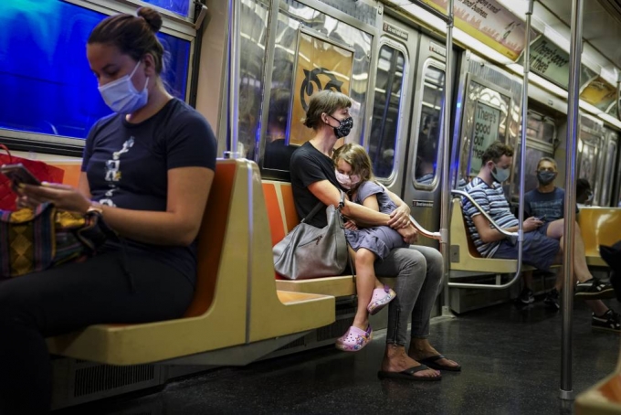 미국 뉴욕의 지하철 안에서 마스크를 쓴 한 여자아이가 엄마의 무릎에 앉아 쉬고 있다. 띄엄띄엄 앉은 승객들 모두 마스크를 착용하고 있다. /AP=뉴시스