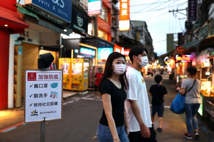 15일 대만 타이베이의 한 야시장에서 시민들이 '마스크를 쓰고 손을 씻고 사회적 거리를 유지하라'는 안내문 앞을 지나고 있다./사진=로이터