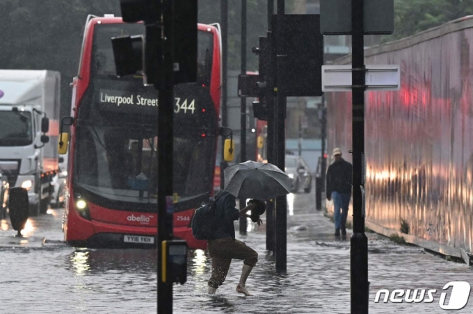 (런던 AFP=뉴스1) 이정후 기자 = 25일(현지시간) 영국 런던에 많은 비가 내려 물에 잠긴 도로를 한 시민이 걸어가고 있다. 이번 폭우로 일부 도로가 폐쇄됐고 버스가 도로에 갇히기도 했다.  (C) AFP=뉴스1  