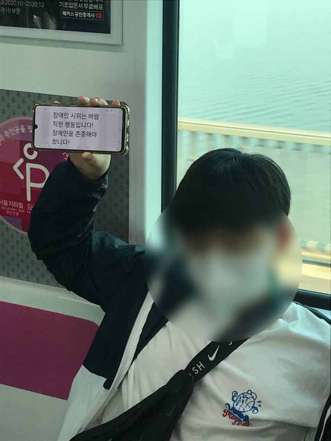 지난 9월 28일 '38차 지하철 출근길 탑니다' 시위 당시  2호선 당산역을 향하는 열차 안에서 한 소년이 시위 응원 문구를 적은 휴대폰 화면을 들어 보이고 있다. /사진제공=전장연