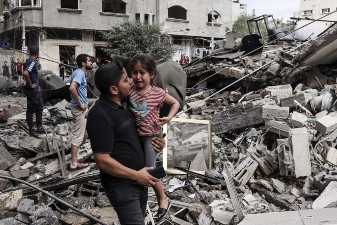7일(현지시간) 팔레스타인인들이 거주하는 가자지구의 가자 시티에서 한 남성이 우는 아이를 안고서 이스라엘의 공격으로 파괴된 건물 앞을 걷고 있다. 이날 팔레스타인 무장 정파 하마스의 이스라엘 공습 이후 이스라엘은 이를 전쟁으로 규정하고 보복 의지를 내보였다. /AFPBBNews=뉴스1