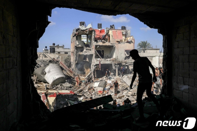 (칸유니스 AFP=뉴스1) 최종일 기자 = 이스라엘과 팔레스타인 가자지구를 통치하고 있는 무장정파 하마스 간 전쟁이 지속되고 있는 가운데 8일(현지시간) 가자지구 남부 칸유니스 캠프에서 한 남성이 이스라엘의 포격으로 벽면에 큰 구멍이 생긴 건물 앞을 지나고 있다. 다른 주민들은 무너진 건물 잔해 속에서 생존자들 수색하고 있다.   ⓒ AFP=뉴스1  Copyright (C) 뉴스1. All rights reserved. 무단 전재 및 재배포,  AI학습 이용 금지.