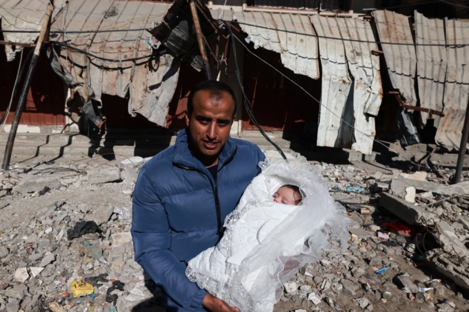 11일(현지시간) 플레스타인 가자지구 남부 라파에서 이스라엘의 폭격으로 파괴된 건물 잔해 위에서 한 남성이 갓 태어난 아기와 함께 사진을 찍기 위해 포즈를 취하고 있다./AFPBBNews=뉴스1