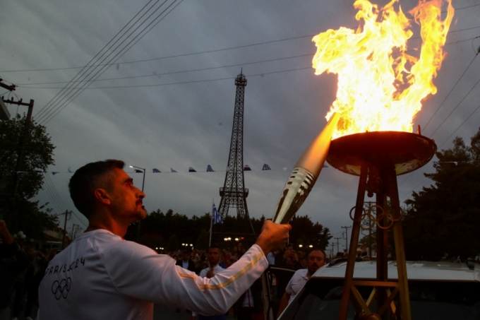 지난 16일 그리스 필리아트라 마을에서 열린 2024 파리 올림픽 성화 봉송에서 전 그리스 축구선수 니코스 림페로풀로스가 에펠탑 모형 앞에서 성화대에 불을 붙이고 있다. /로이터=뉴스1